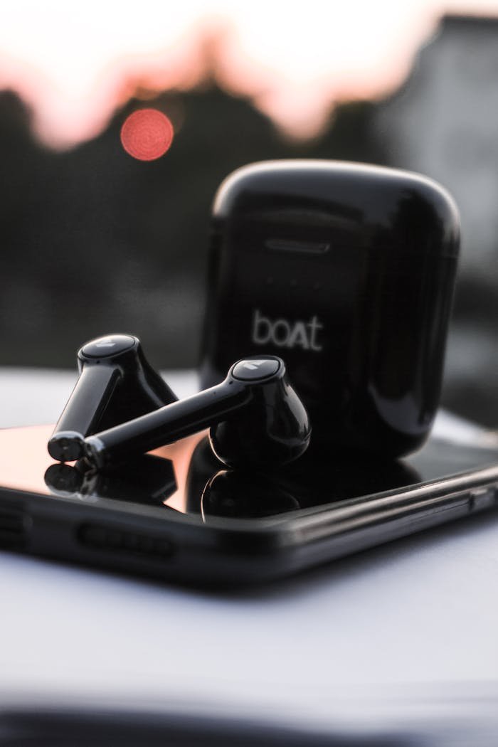 Sleek black wireless earbuds on a smartphone with a blurred outdoor background.