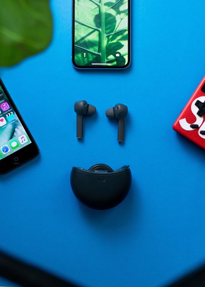 Flat lay of wireless headphones and smartphones on a blue background, showcasing modern tech devices.